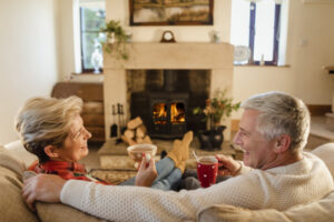 The Basics of Winter Indoor Air Quality - Mature couple sat infront of a fire drinking hot chocalate from mugs.