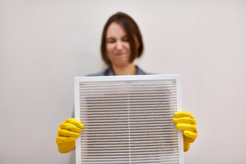 Dirty hvac air filter being held by a woman with yellow gloves