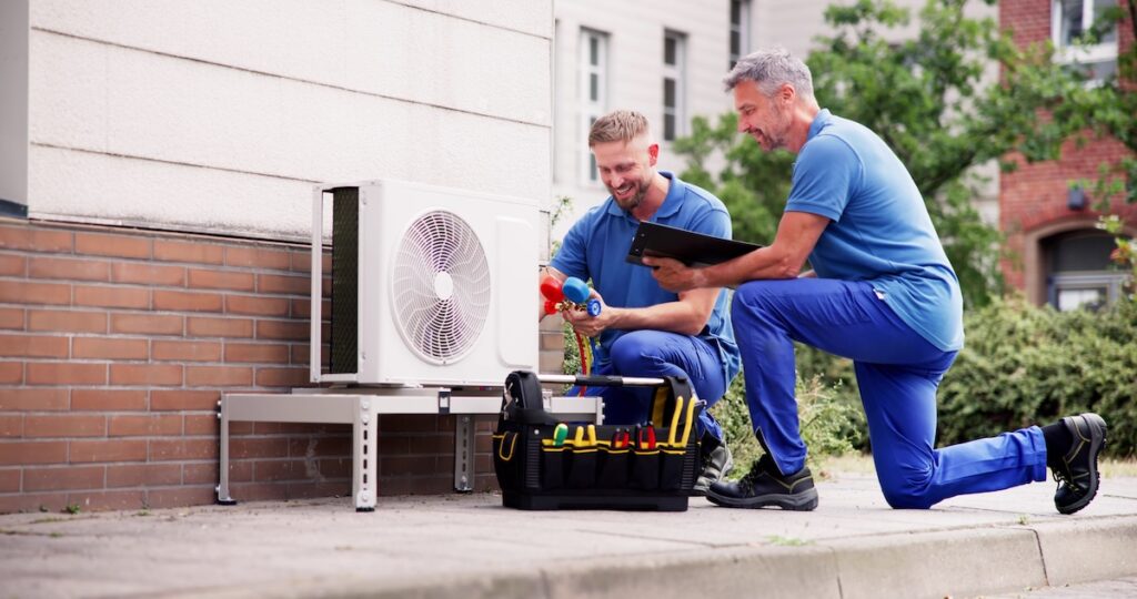 Heat pump outside with two technicians inspecting