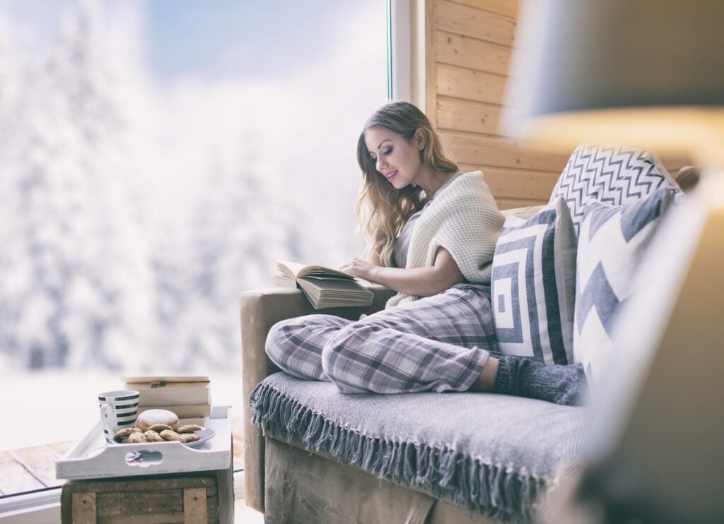 Young woman reading in warm house while there is snow outside
