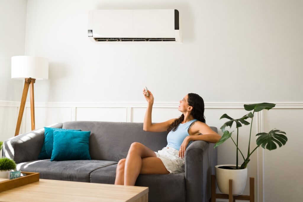 Happy woman using her new air conditioning Woman sitting on the couch and using the remote to change the room temperature of the ac unit
