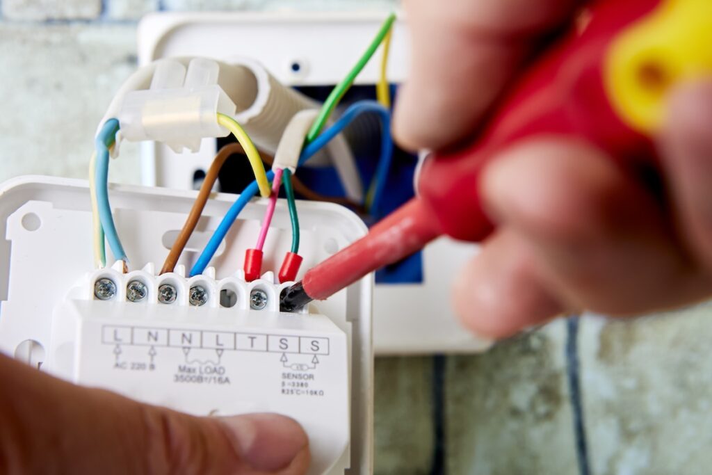 Connecting colored wires to terminals of thermostat for floor heating. Electrician connecting colored wires to terminals of wall mounted thermostat